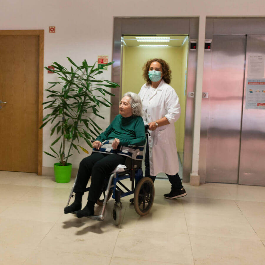 Sra. idosa de cadeira de rodas empurrada por enfermeira